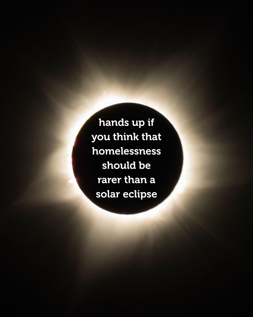 A solar eclipse with a bright corona is in the background. Over the dark center, white text reads: "hands up if you think that homelessness should be rarer than a solar eclipse.