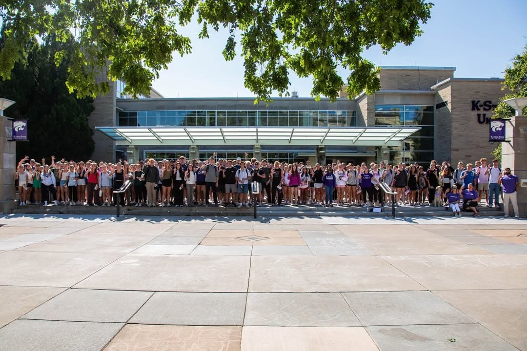 A large group of people standing in front of a building with "K-State" visible.
