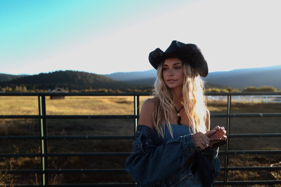 A woman wearing a cowboy hat standing in a golden field in the California countryside during golden hour.